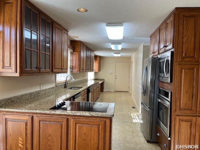 kitchen with light stone counters, light floors, appliances with stainless steel finishes, and a sink