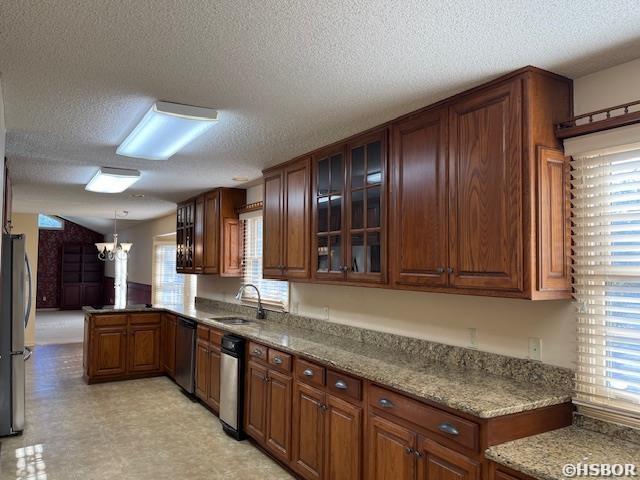 kitchen with a sink, freestanding refrigerator, a peninsula, glass insert cabinets, and a chandelier