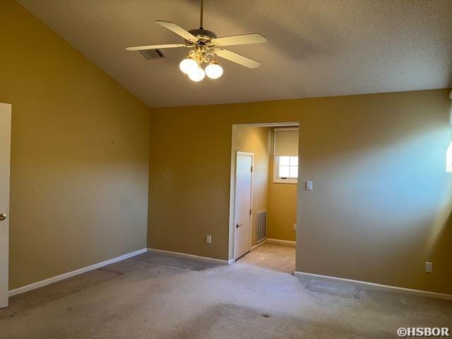 carpeted empty room with visible vents, lofted ceiling, a ceiling fan, a textured ceiling, and baseboards