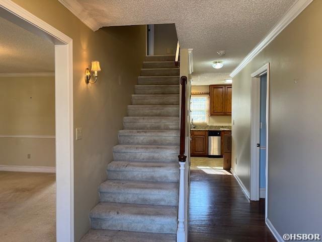 stairway featuring a textured ceiling, wood finished floors, baseboards, and ornamental molding