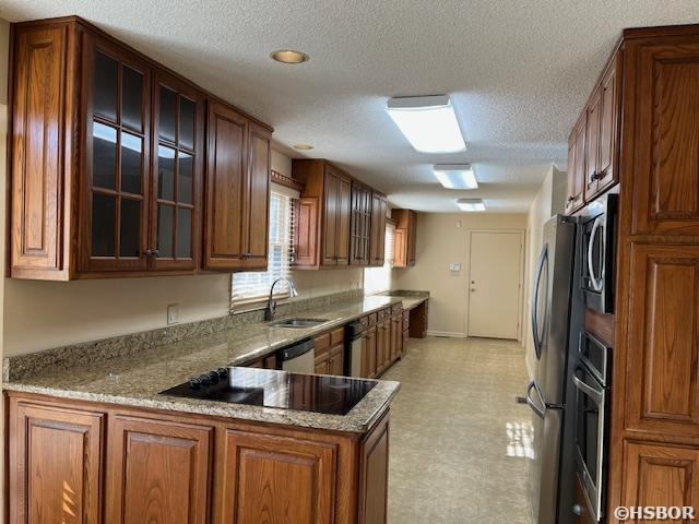 kitchen with light stone counters, a peninsula, brown cabinetry, glass insert cabinets, and light floors