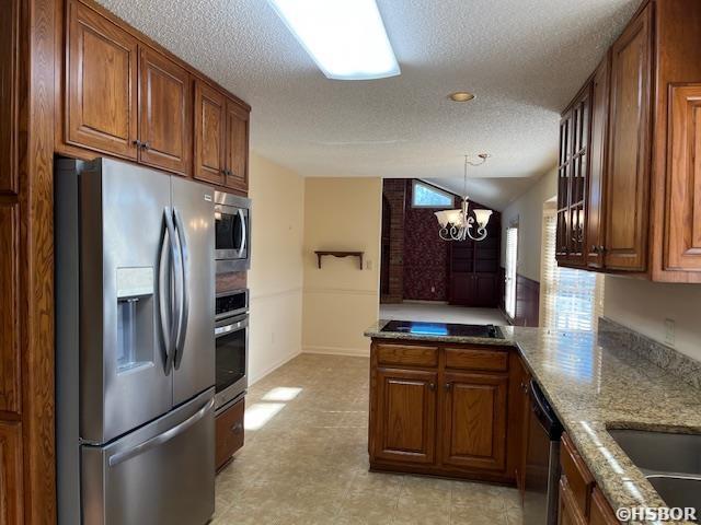 kitchen with brown cabinets, a notable chandelier, stainless steel appliances, a peninsula, and lofted ceiling