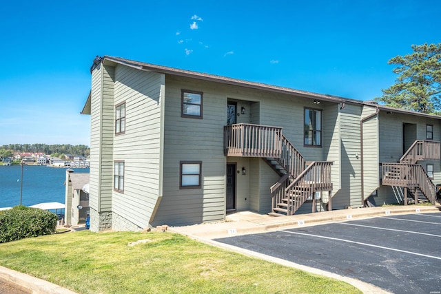 exterior space with uncovered parking, a front lawn, stairway, and a water view