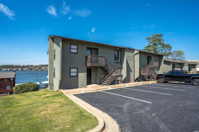 view of front facade with stairs, uncovered parking, a water view, and a front yard