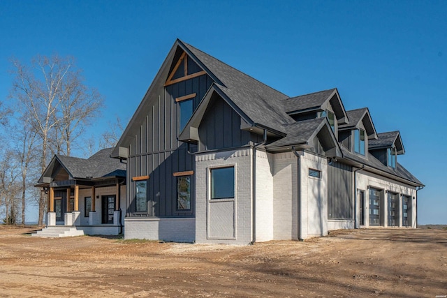 view of side of property featuring covered porch, roof with shingles, board and batten siding, and brick siding