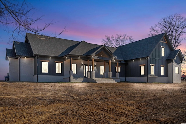 modern farmhouse style home with covered porch, roof with shingles, board and batten siding, and brick siding