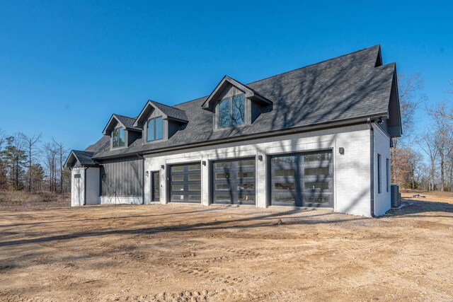 view of front facade featuring brick siding, central air condition unit, a shingled roof, a garage, and driveway