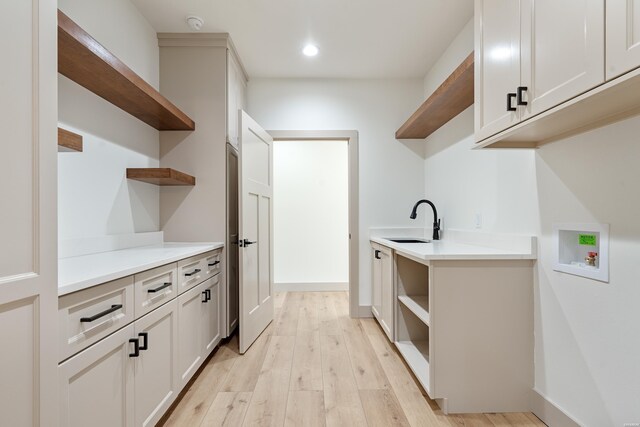 interior space featuring hookup for a washing machine, recessed lighting, cabinet space, light wood-style floors, and a sink