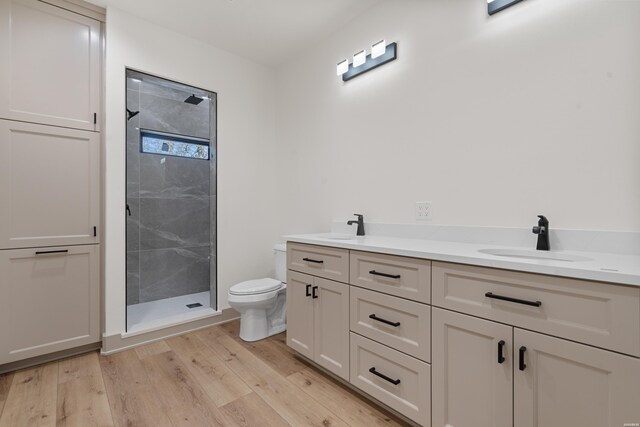 full bathroom featuring double vanity, toilet, a sink, a shower stall, and wood finished floors