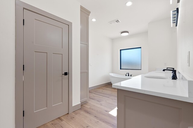 bathroom with double vanity, visible vents, a soaking tub, wood finished floors, and a sink