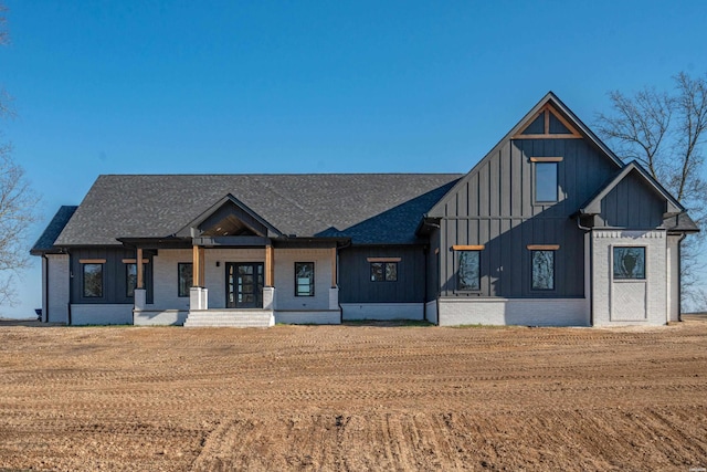 modern farmhouse with a porch, board and batten siding, a front lawn, and brick siding