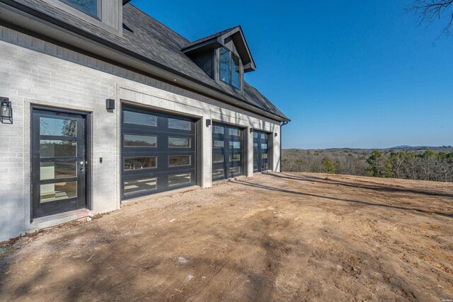 exterior space with dirt driveway, brick siding, and a shingled roof