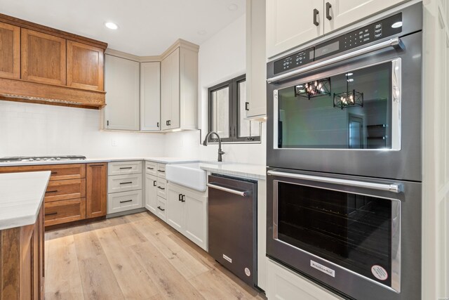 kitchen with white cabinets, appliances with stainless steel finishes, light countertops, light wood-type flooring, and a sink