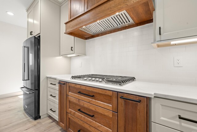 kitchen with high end black fridge, premium range hood, white cabinets, decorative backsplash, and stainless steel gas stovetop