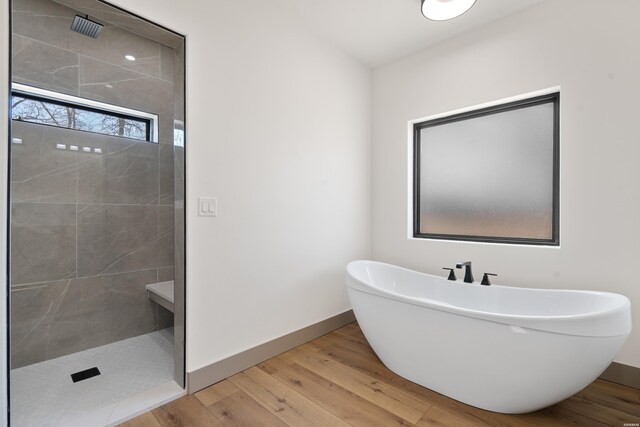 bathroom with a walk in shower, a freestanding tub, wood finished floors, and baseboards