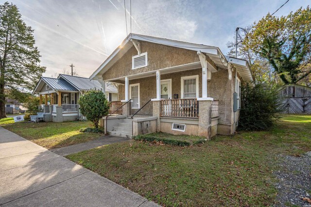 bungalow-style house with covered porch, a front yard, and stucco siding