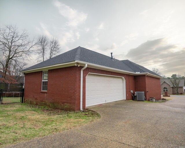 view of side of property with an attached garage, roof with shingles, central AC unit, and brick siding