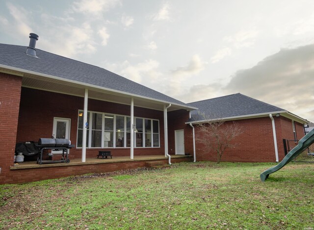 rear view of property with roof with shingles, brick siding, and a lawn