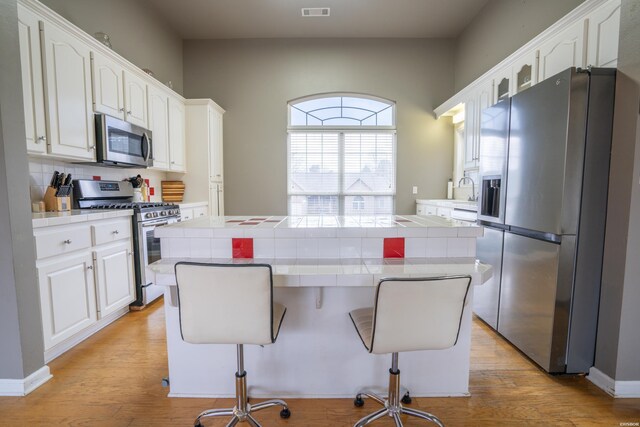 kitchen with visible vents, tile counters, a breakfast bar area, stainless steel appliances, and white cabinetry