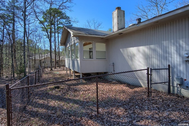 view of side of home featuring a sunroom, a chimney, and fence