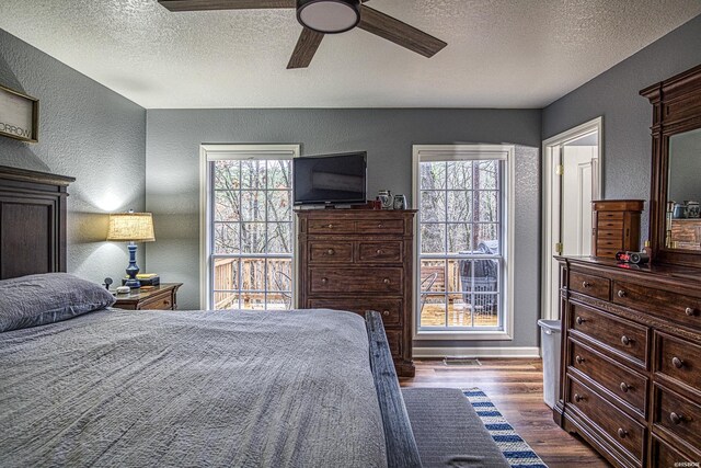 bedroom with multiple windows, dark wood finished floors, and a textured wall