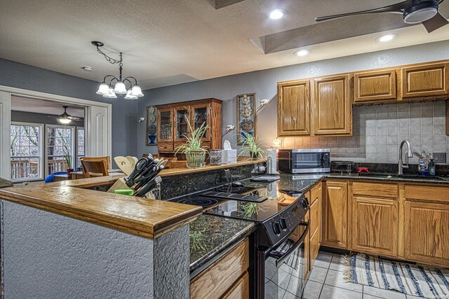 kitchen featuring ceiling fan with notable chandelier, black electric range, brown cabinets, decorative backsplash, and dark countertops