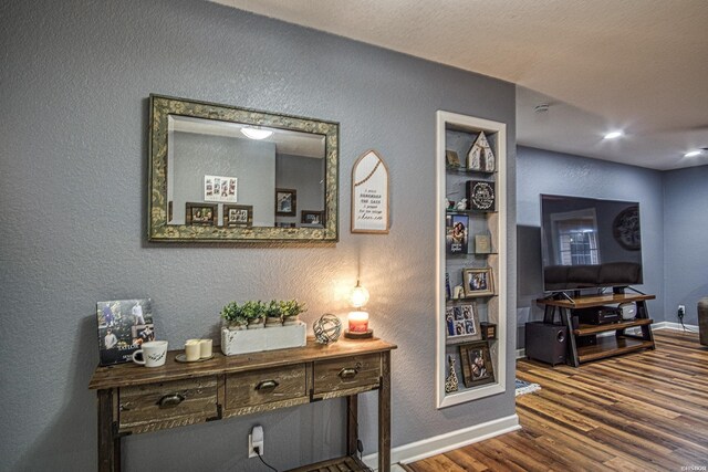 corridor with baseboards, dark wood finished floors, built in features, and a textured wall