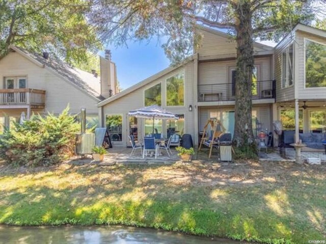 rear view of house with a chimney, a patio area, a lawn, and a balcony