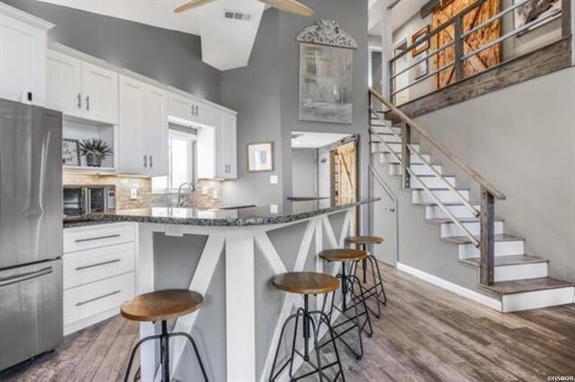 kitchen with visible vents, freestanding refrigerator, dark stone countertops, wood finished floors, and a kitchen bar