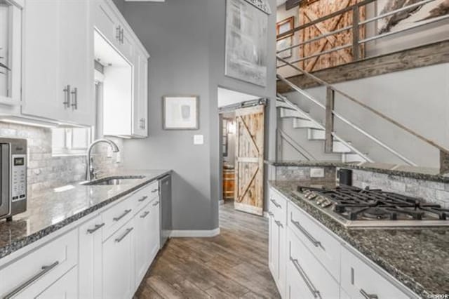 kitchen with tasteful backsplash, a barn door, stainless steel appliances, white cabinetry, and a sink