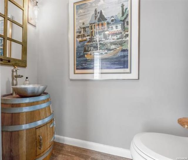 half bathroom with toilet, baseboards, wood finished floors, and vanity