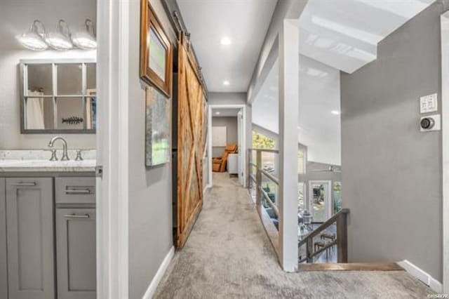 corridor with a barn door, baseboards, light colored carpet, an upstairs landing, and a sink