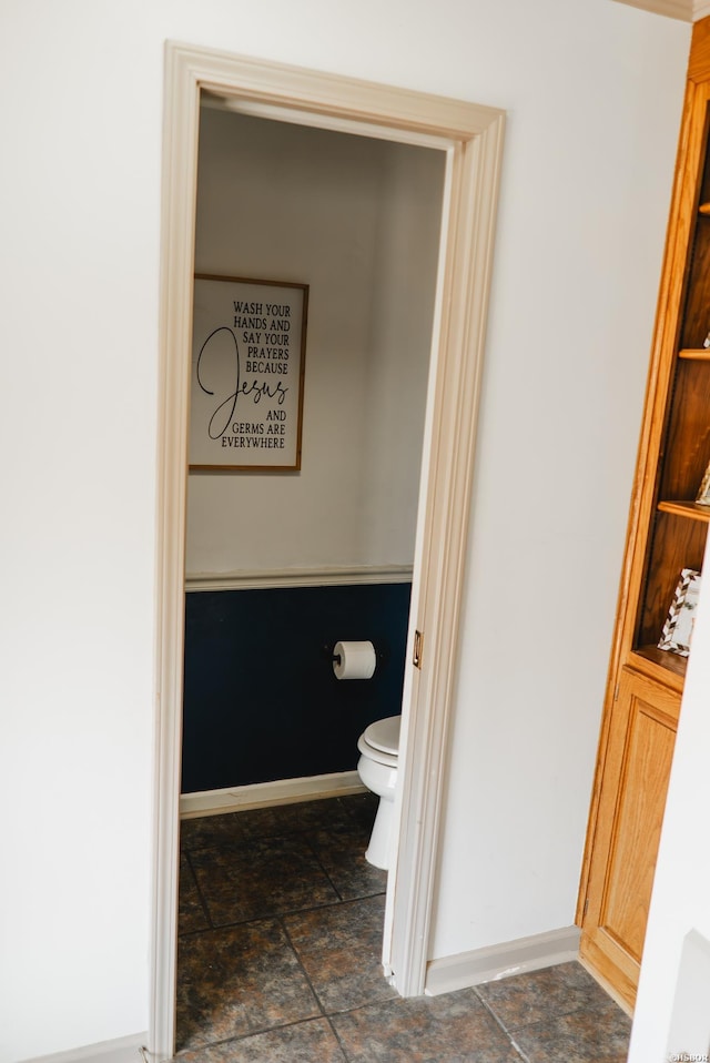 bathroom featuring stone finish flooring, baseboards, and toilet