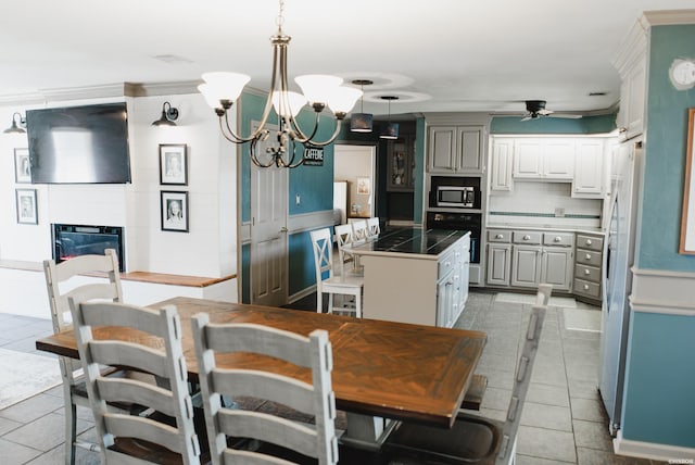 kitchen with light tile patterned floors, ceiling fan with notable chandelier, appliances with stainless steel finishes, backsplash, and a glass covered fireplace