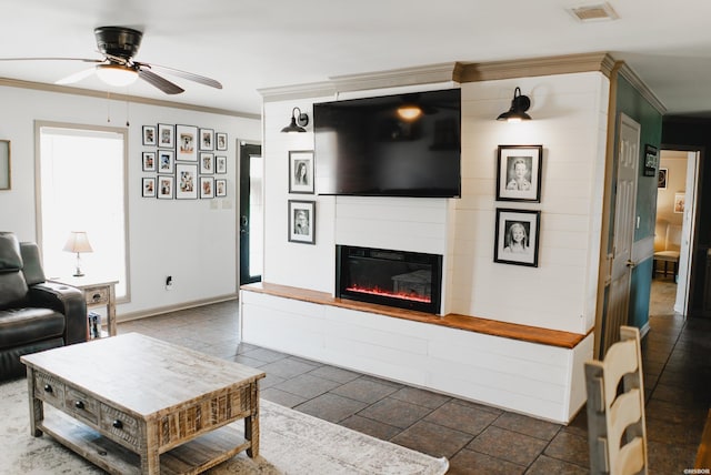 living room featuring ceiling fan, visible vents, baseboards, a glass covered fireplace, and crown molding