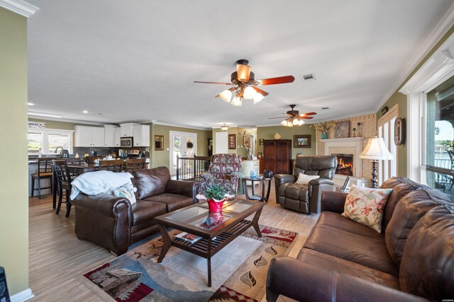 living area featuring ornamental molding, a brick fireplace, visible vents, and light wood-style flooring