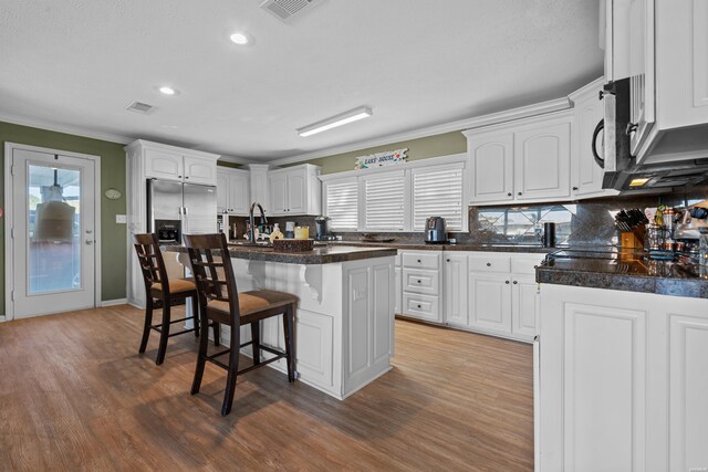 kitchen featuring a breakfast bar area, dark countertops, a kitchen island with sink, and white cabinets