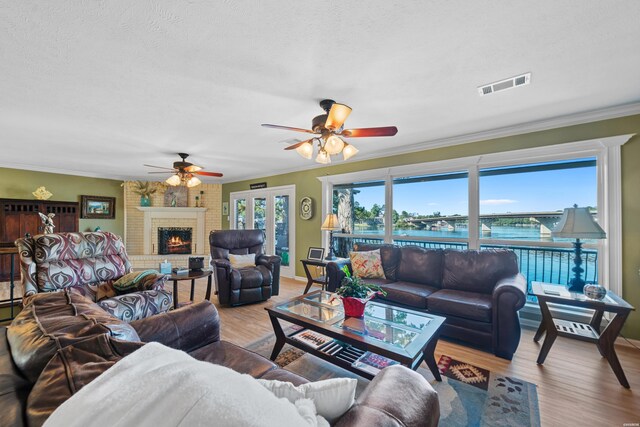 living area featuring a brick fireplace, visible vents, a water view, crown molding, and light wood-style floors