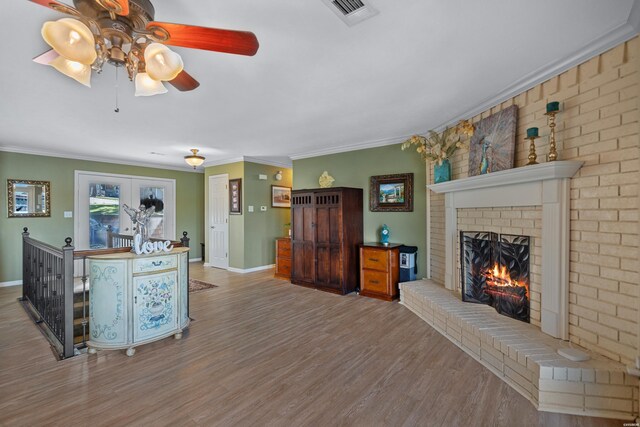 interior space with light wood finished floors, visible vents, ornamental molding, a brick fireplace, and baseboards