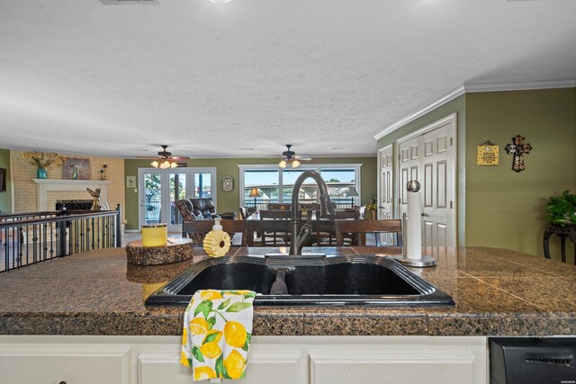 kitchen featuring a brick fireplace, white cabinets, a sink, and a textured ceiling