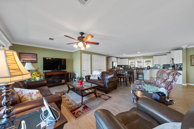 living room with light wood-style floors, visible vents, ornamental molding, and a ceiling fan