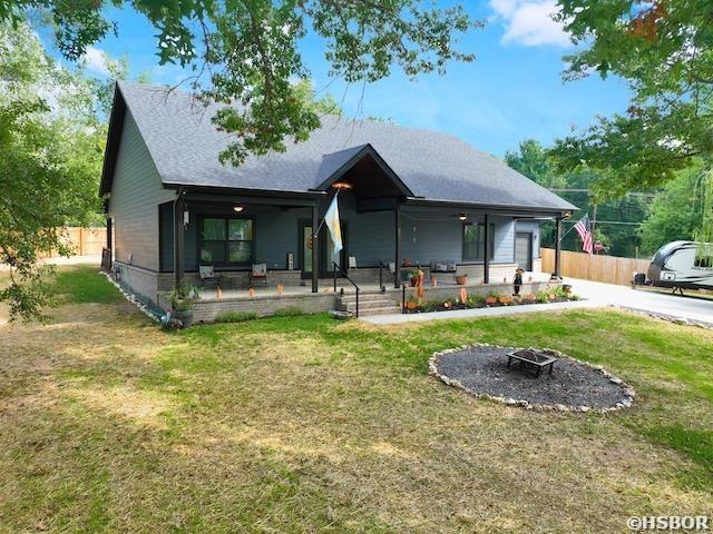 view of front facade with a porch, a front yard, fence, and a fire pit