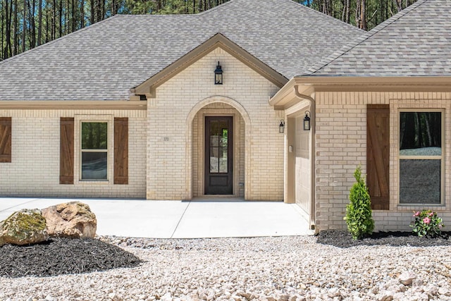 view of exterior entry featuring brick siding and a shingled roof