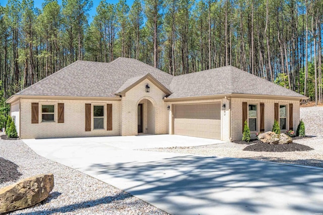 view of front of house with brick siding, an attached garage, a shingled roof, and driveway