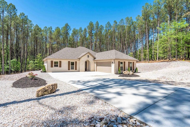view of front facade featuring a garage, stucco siding, a forest view, and concrete driveway
