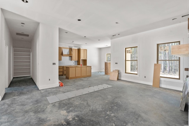 unfurnished living room featuring a healthy amount of sunlight, stairs, baseboards, and unfinished concrete floors