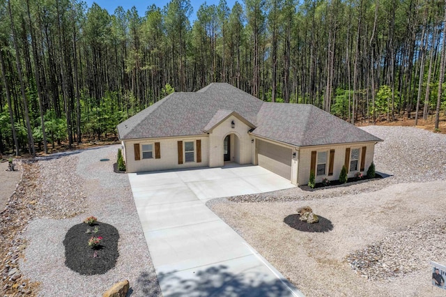 view of front facade with driveway, roof with shingles, a wooded view, and a garage