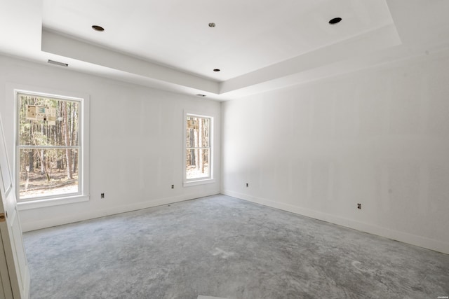 spare room featuring a raised ceiling, baseboards, and unfinished concrete floors