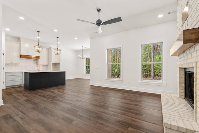 unfurnished living room featuring a fireplace, a wealth of natural light, baseboards, and ceiling fan with notable chandelier