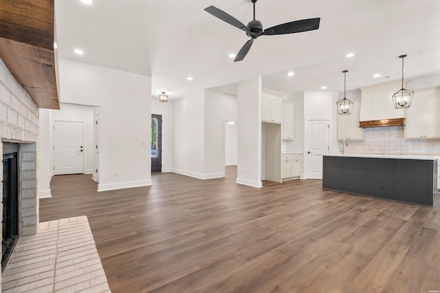 unfurnished living room featuring recessed lighting, wood finished floors, baseboards, a brick fireplace, and ceiling fan